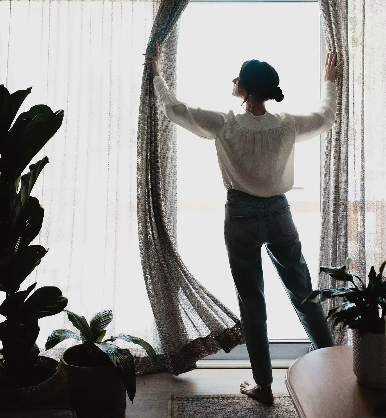 A woman opening the curtains in a softly lit interior